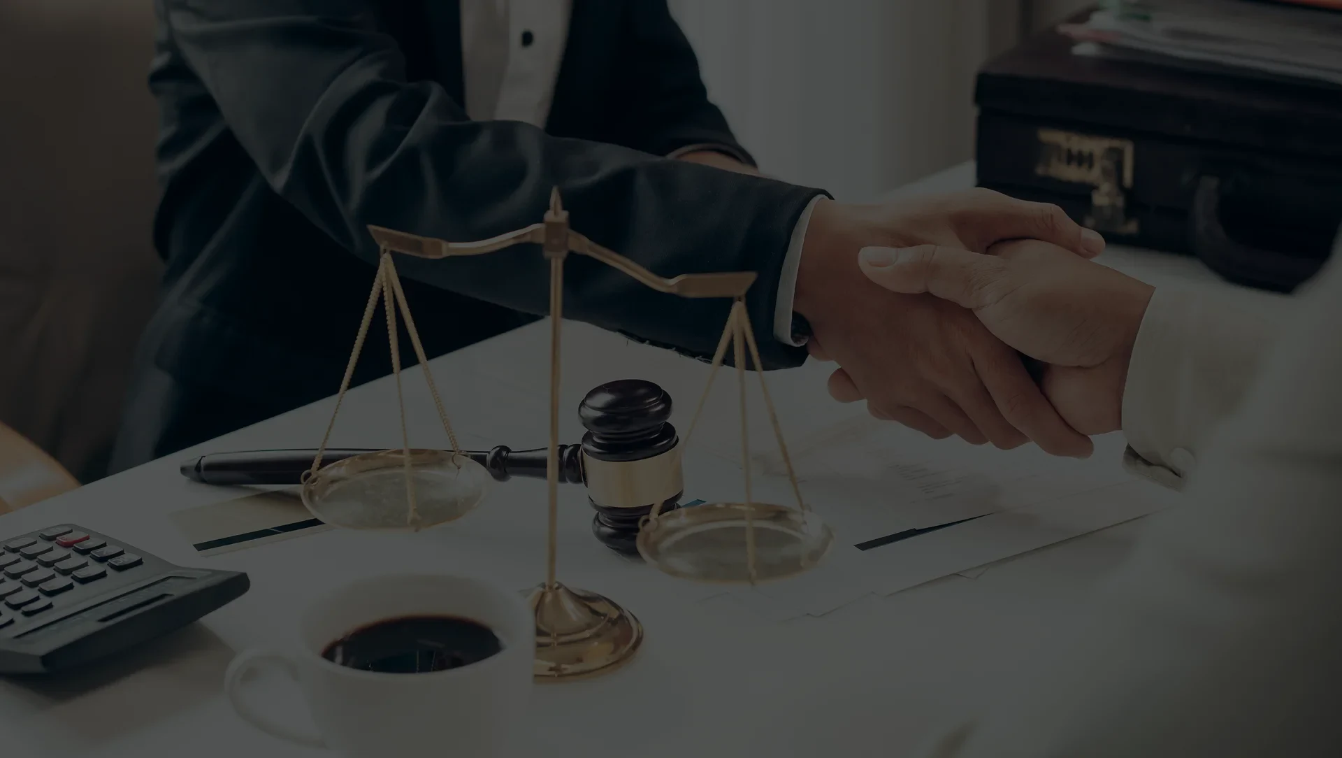 Two people shake hands over a desk with a gavel and scales of justice, symbolizing a legal agreement or partnership.